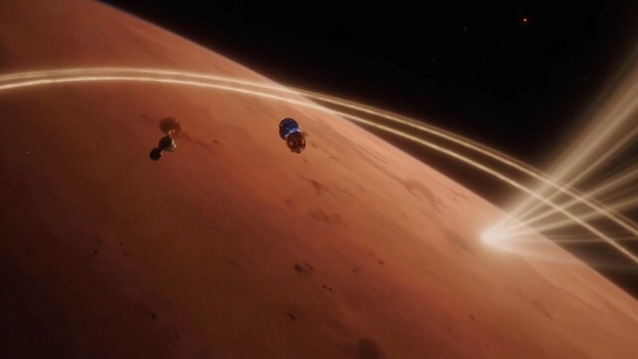 Artist rendering of two small blue-and-gold spacecraft orbiting Mars with visible solar wind particle streams interacting with the planet's magnetosphere