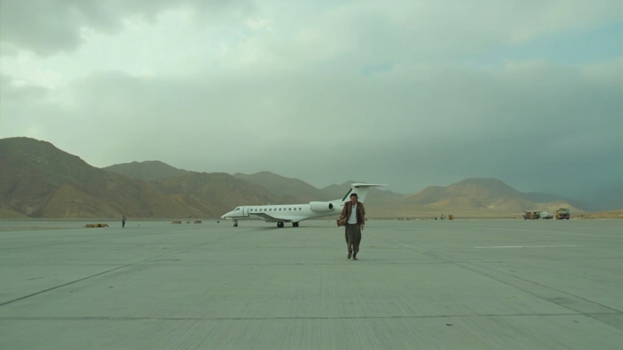 A solitary figure walking across an airport tarmac toward a small chartered aircraft under an overcast sky in Kabul