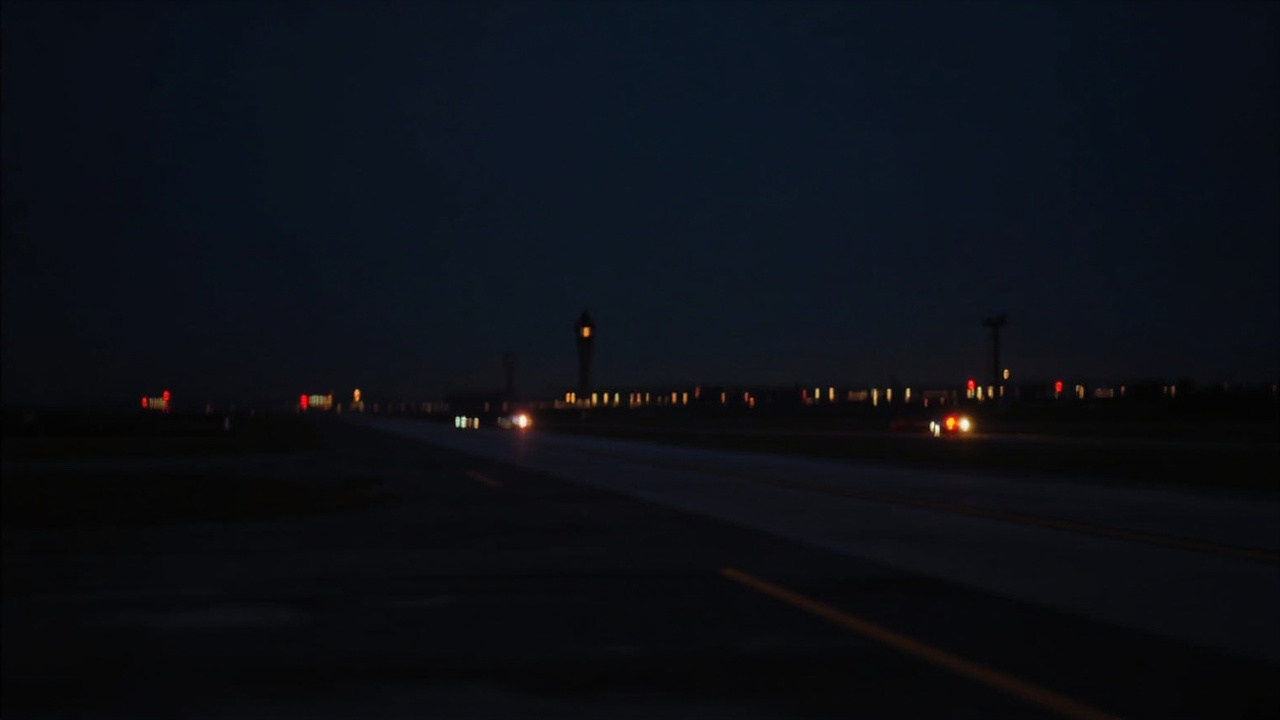 LaGuardia Airport runway at night, emergency vehicle lights visible in the distance, control tower silhouetted against dark sky