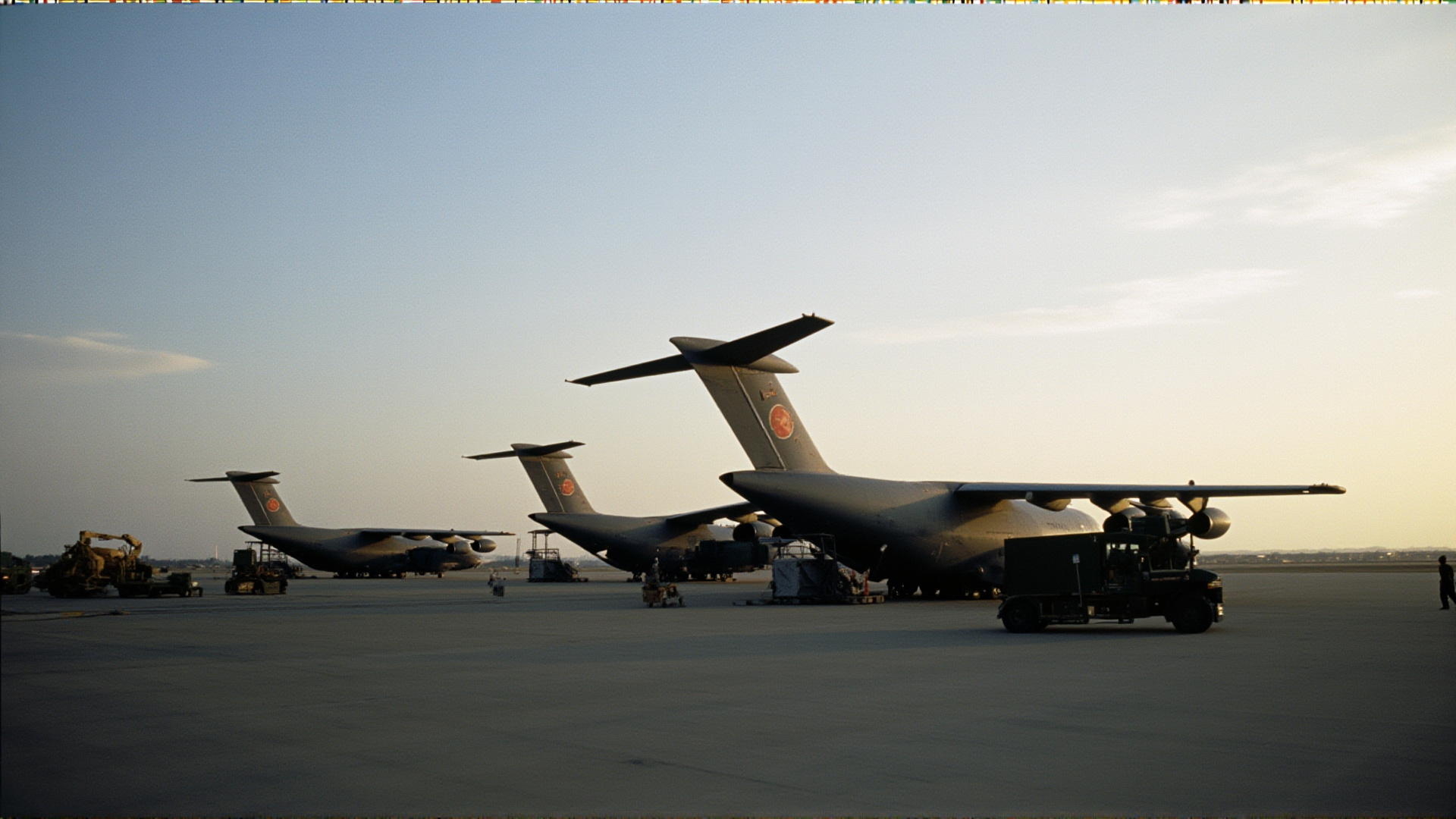Military transport aircraft on a tarmac, cargo ramps down, equipment staged nearby, dawn light, operational readiness