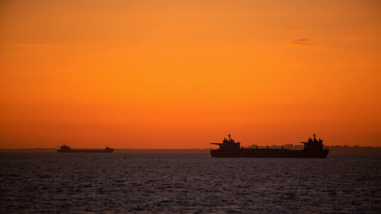 Oil tanker ships at sea at dusk, silhouettes against orange sky