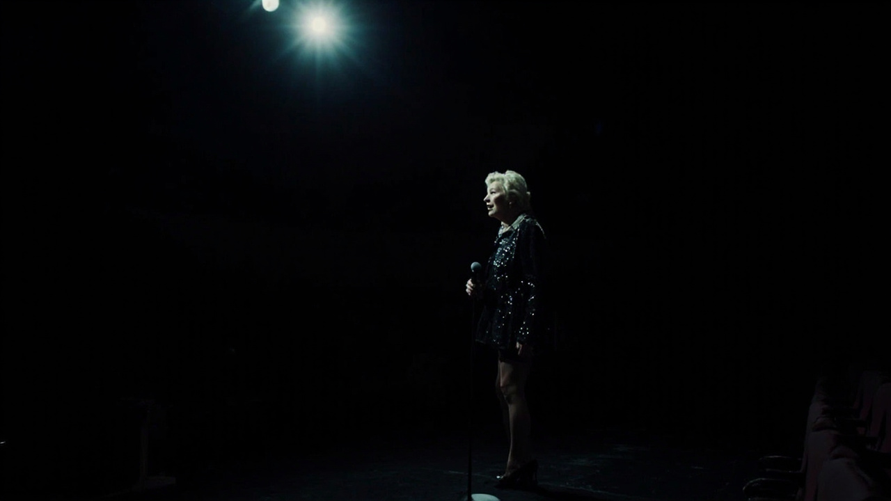 Jean Smart in character as Deborah Vance under bright stage lights with a microphone and sequined outfit