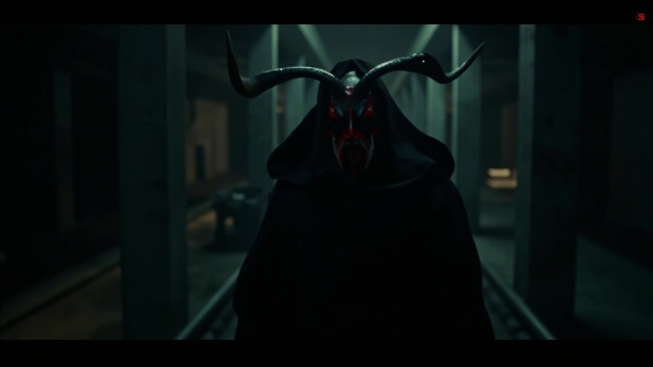 An animation still of a red-skinned horned figure wielding a double-bladed lightsaber in a dark industrial setting