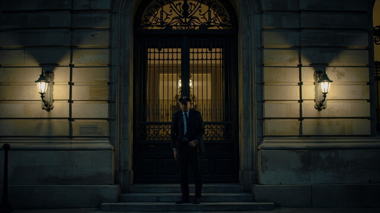 Facade of the Paris Palais de Justice at dusk, iron gates closed, a lone security officer on the steps.