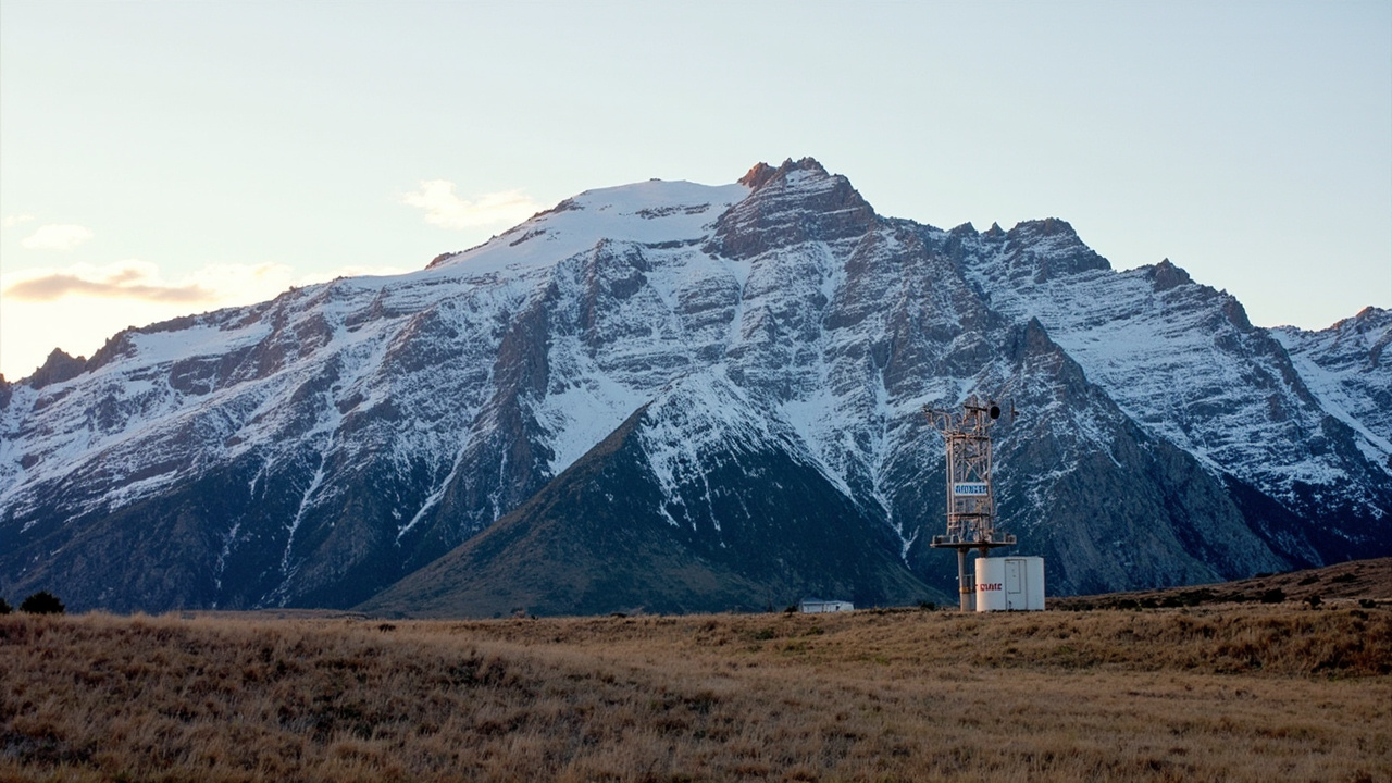A rocky mountain ridge with patchy remnants of snow only at the highest elevations, a bare SNOTEL snow-measurement station in the foreground, late afternoon light, Colorado Rockies.