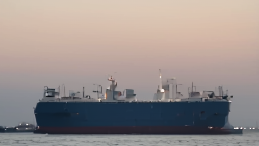 Large crude oil tanker at anchor off a hazy Indian coastline, the sun low over the Arabian Sea, fishermen in a wooden boat in foreground.