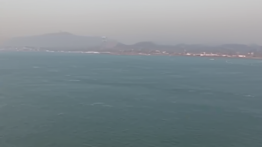 Aerial view of the Strait of Hormuz with a single tanker visible against empty sea lanes, Iranian coast in distance