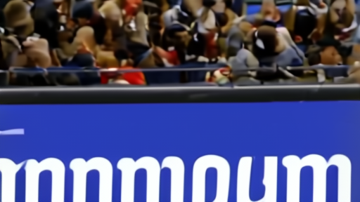 Wembanyama in street clothes on the Spurs bench at Moda Center, towel over his shoulders, crowd in background.