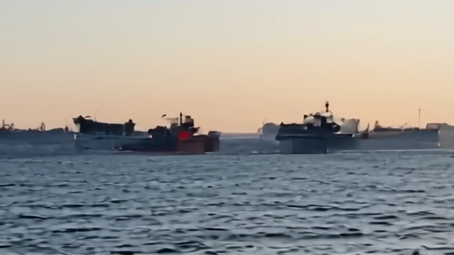 A line of very large crude carriers anchored offshore, gulf coastline visible in the distance.