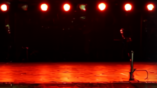 An empty country-music club stage with a single guitar on a stand and a row of dim stage lights overhead.