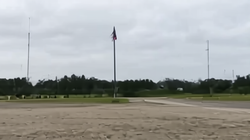 An empty parade square at Ramstein Air Base under low cloud, two American flags at half-staff