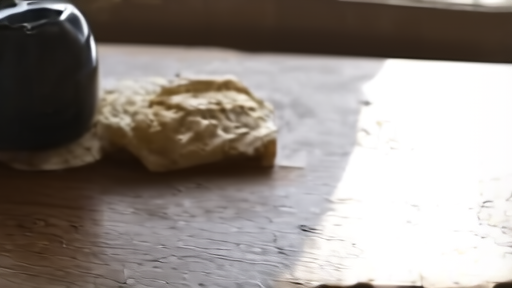 A bread loaf and a working person's hands at a long communal table set in soft window light