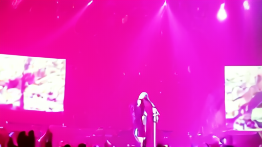Olivia Rodrigo on stage during the Unraveled Tour singing into a microphone with stadium lighting and a crowd in the foreground.