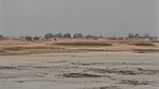 A damaged airport tarmac sits near distant fuel tanks under a dust-colored sky.