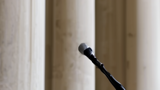 Senator Lisa Murkowski mid-sentence at a Senate hallway scrum with raised microphones and Capitol marble in soft focus