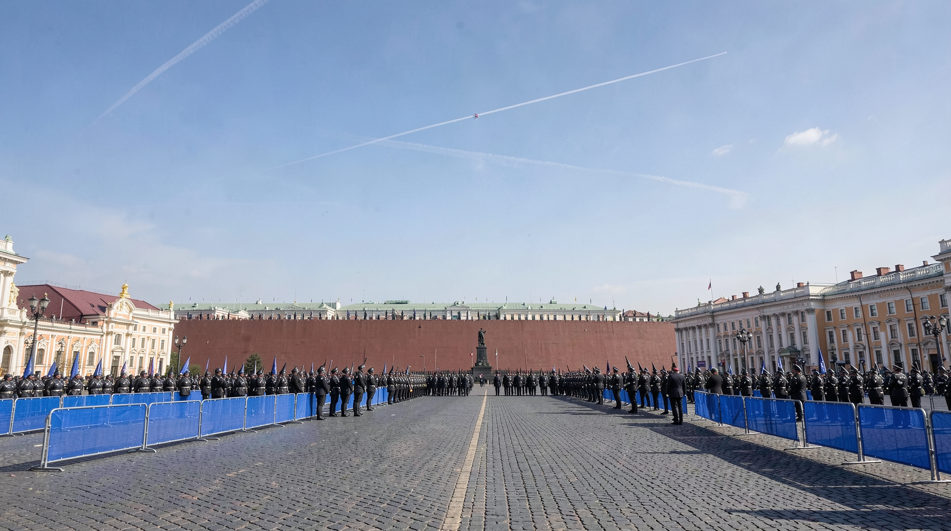 Red Square mostly empty at noon under a single jet contrail, parade barriers up but troops thin on the ground