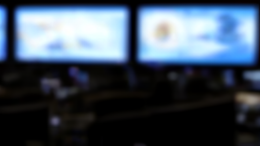 A trading floor with empty workstations and multiple flat screens showing market activity in low light