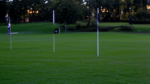 An empty championship golf course at dusk with flagsticks on greens and clubhouse lights visible in the distance