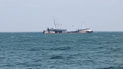 Oil tanker anchored in open water with military vessel visible in the background