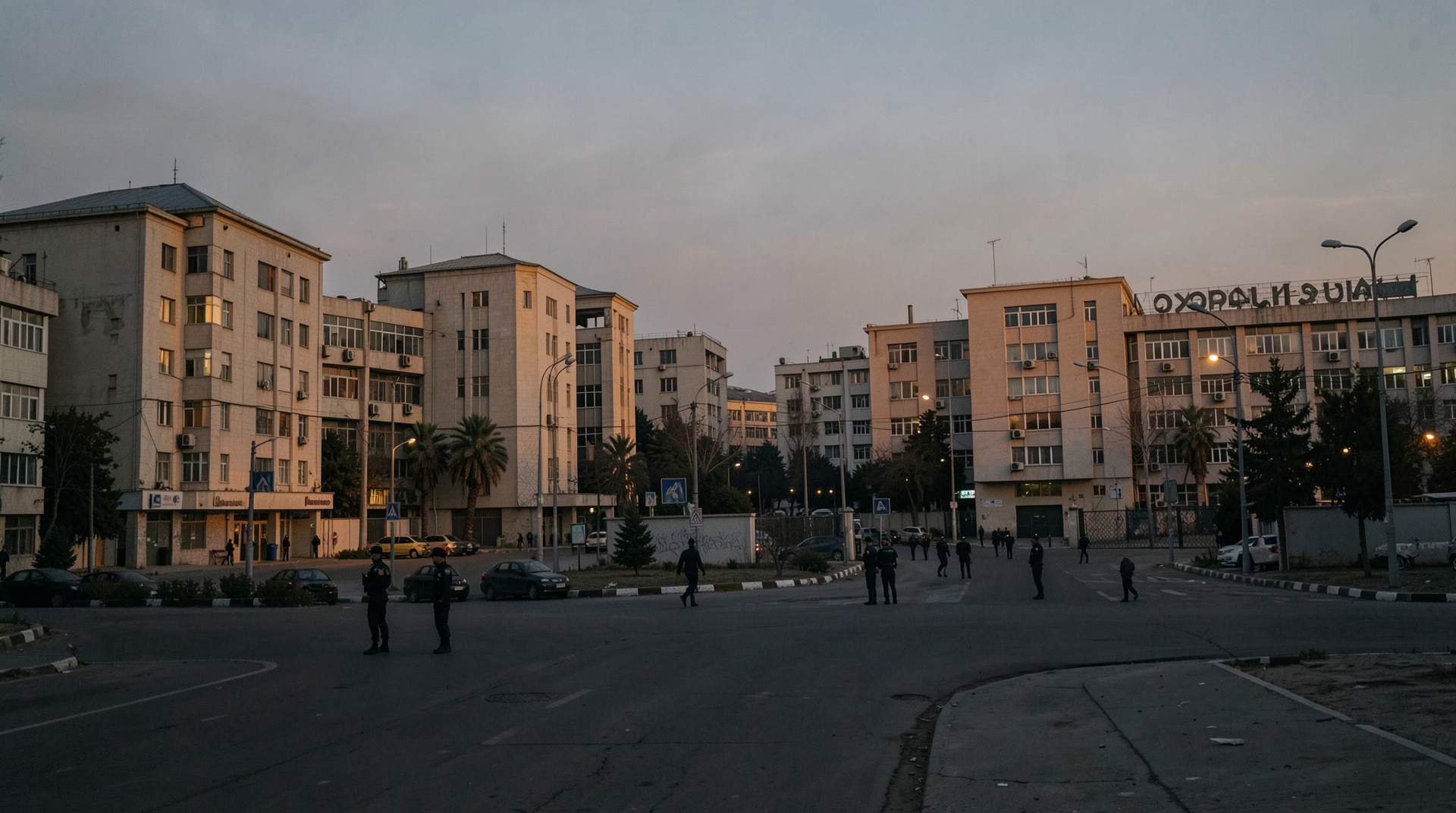 The Tehran government quarter at dusk, security personnel in mid-distance, the low light catching the rooflines of the ministerial buildings.