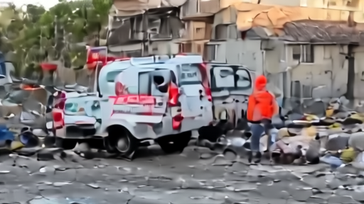 The wreckage of an ambulance with crescent insignia in a damaged street in southern Lebanon, with first responders examining the scene.