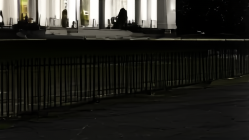 A North Lawn fence of the White House at night, security floodlights illuminating empty pavement, no people.