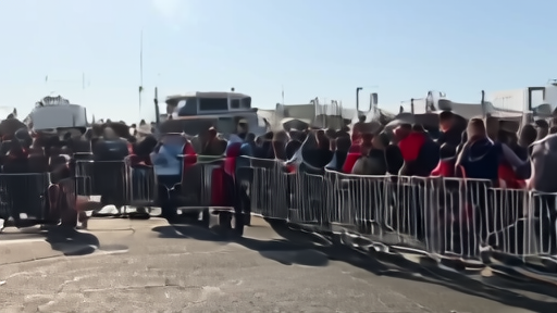 Fans waiting outside a sunny stadium gate with water bottles and medical volunteers nearby
