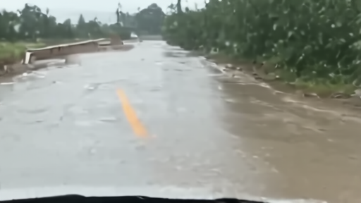 A Texas Gulf Coast road filling with rainwater as a phone shows flood alerts without a named storm.