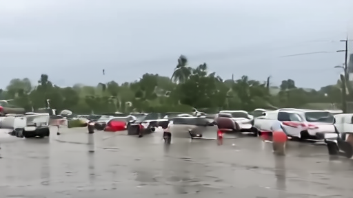 A flooded south Texas street under heavy rain, a resident wading past stalled cars beneath low disorganized storm clouds