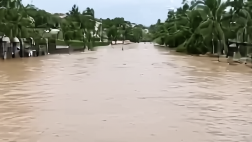 A coastal street floods while a phone alert says Arthur has been downgraded