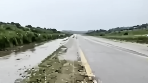 Coastal road after rain with flood-gauge markings and weather-service briefing on a tablet